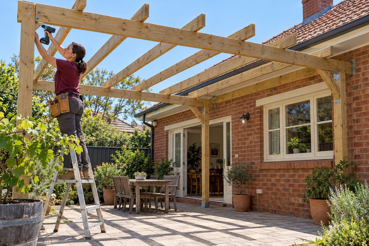 Pergolas, Adelaide: carpenter on a stepladder fixing a rafter on a new timber pergola frame beside a red-brick bungalow